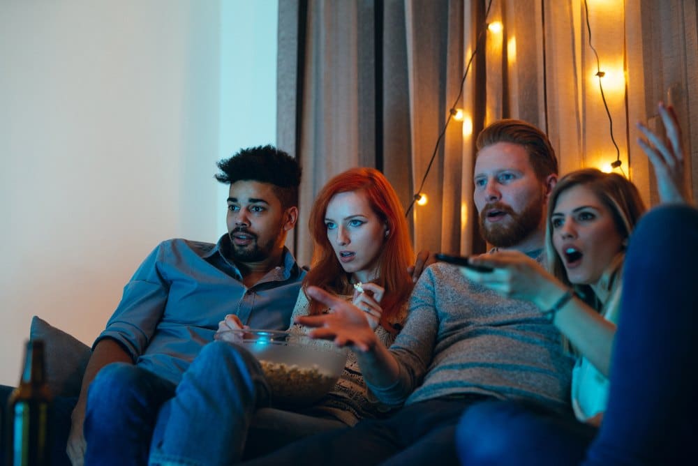 Four friends watching a scary movie on the couch.